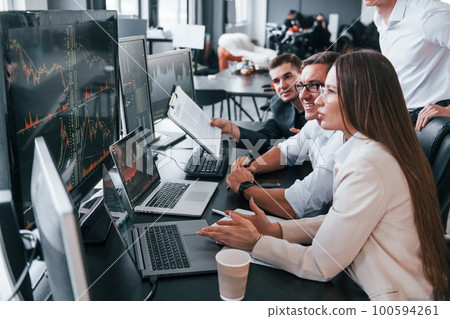 Analysing information. Team of stockbrokers works in modern office with many display screens Analysing information. Team of stockbrokers works in modern office with many display screens 100594261