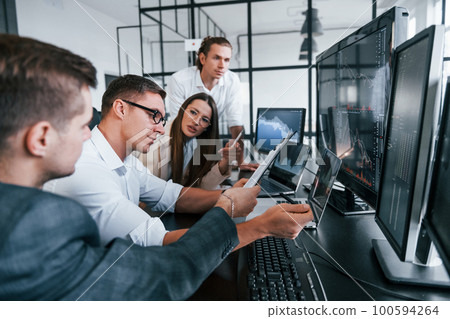 Analysing information. Team of stockbrokers works in modern office with many display screens Analysing information. Team of stockbrokers works in modern office with many display screens 100594264
