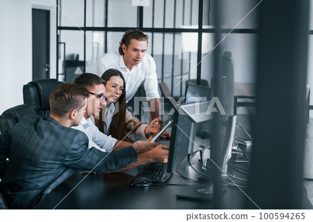 Analysing information. Team of stockbrokers works in modern office with many display screens Analysing information. Team of stockbrokers works in modern office with many display screens 100594265