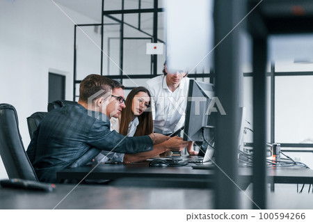 Sitting by the table. Team of stockbrokers works in modern office with many display screens Sitting by the table. Team of stockbrokers works in modern office with many display screens 100594266