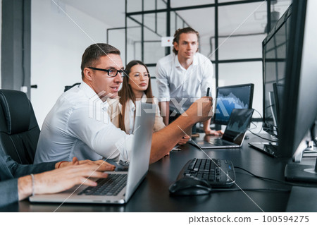 Sitting by the table. Team of stockbrokers works in modern office with many display screens Sitting by the table. Team of stockbrokers works in modern office with many display screens 100594275