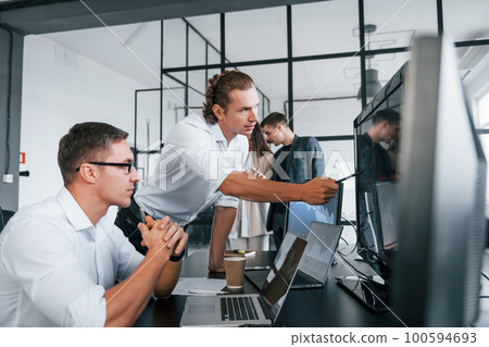 Sitting by the table. Team of stockbrokers works in modern office with many display screens Sitting by the table. Team of stockbrokers works in modern office with many display screens 100594693