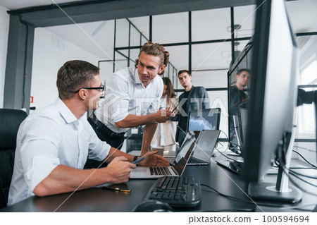 Sitting by the table. Team of stockbrokers works in modern office with many display screens Sitting by the table. Team of stockbrokers works in modern office with many display screens 100594694