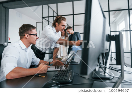 Guy in glasses concentrated at work. Team of stockbrokers is in modern office with many display screens 100594697