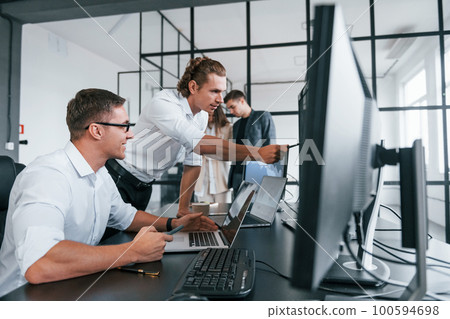 Guy in glasses concentrated at work. Team of stockbrokers is in modern office with many display screens Guy in glasses concentrated at work. Team of stockbrokers is in modern office with many display screens 100594698