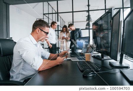 Guy in glasses concentrated at work. Team of stockbrokers is in modern office with many display screens Guy in glasses concentrated at work. Team of stockbrokers is in modern office with many display screens 100594703