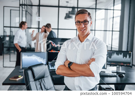 Guy standing in front of people. Team of stockbrokers works in modern office with many display screens Guy standing in front of people. Team of stockbrokers works in modern office with many display screens 100594704