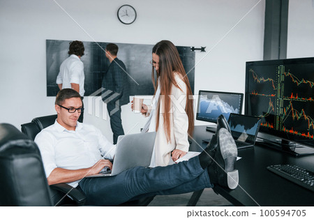 Woman and man have conversation. Team of stockbrokers works in modern office with many display screens Woman and man have conversation. Team of stockbrokers works in modern office with many display screens 100594705