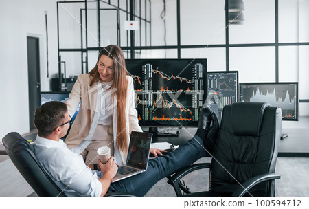 Woman and man have conversation. Team of stockbrokers works in modern office with many display screens Woman and man have conversation. Team of stockbrokers works in modern office with many display screens 100594712