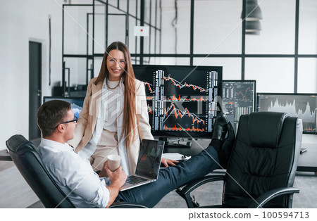 Woman and man have conversation. Team of stockbrokers works in modern office with many display screens Woman and man have conversation. Team of stockbrokers works in modern office with many display screens 100594713