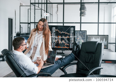 Woman and man have conversation. Team of stockbrokers works in modern office with many display screens Woman and man have conversation. Team of stockbrokers works in modern office with many display screens 100594714