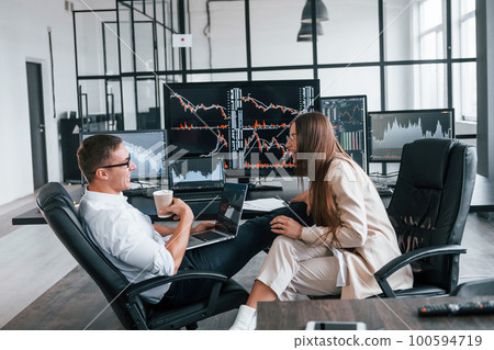 Woman and man have conversation. Team of stockbrokers works in modern office with many display screens Woman and man have conversation. Team of stockbrokers works in modern office with many display screens 100594719