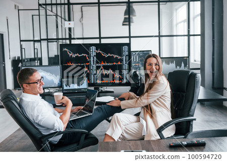 Woman and man have conversation. Team of stockbrokers works in modern office with many display screens Woman and man have conversation. Team of stockbrokers works in modern office with many display screens 100594720
