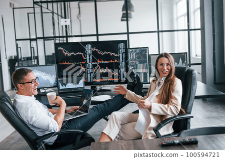 Woman and man have conversation. Team of stockbrokers works in modern office with many display screens Woman and man have conversation. Team of stockbrokers works in modern office with many display screens 100594721