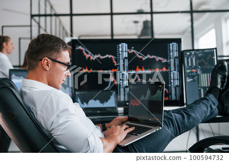 Guy in glasses concentrated at work. Team of stockbrokers is in modern office with many display screens Guy in glasses concentrated at work. Team of stockbrokers is in modern office with many display screens 100594732