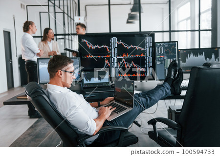 Guy in glasses concentrated at work. Team of stockbrokers is in modern office with many display screens Guy in glasses concentrated at work. Team of stockbrokers is in modern office with many display screens 100594733