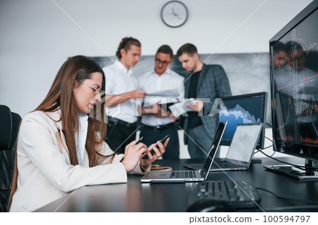 Woman sits in front of laptop and displays. Team of stockbrokers works in modern office with many display screens Woman sits in front of laptop and displays. Team of stockbrokers works in modern office with many display screens 100594797