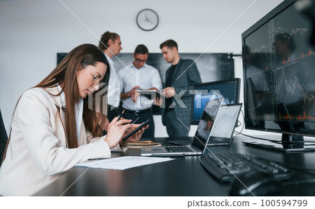 Woman sits in front of laptop and displays. Team of stockbrokers works in modern office with many display screens Woman sits in front of laptop and displays. Team of stockbrokers works in modern office with many display screens 100594799