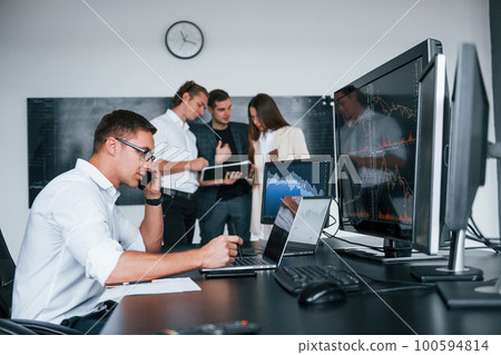 Man uses laptop. Team of stockbrokers works in modern office with many display screens Man uses laptop. Team of stockbrokers works in modern office with many display screens 100594814