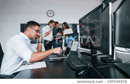 Man uses laptop. Team of stockbrokers works in modern office with many display screens Man uses laptop. Team of stockbrokers works in modern office with many display screens 100594816