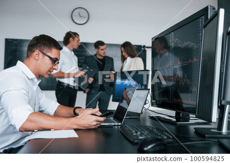 Man uses laptop. Team of stockbrokers works in modern office with many display screens Man uses laptop. Team of stockbrokers works in modern office with many display screens 100594825