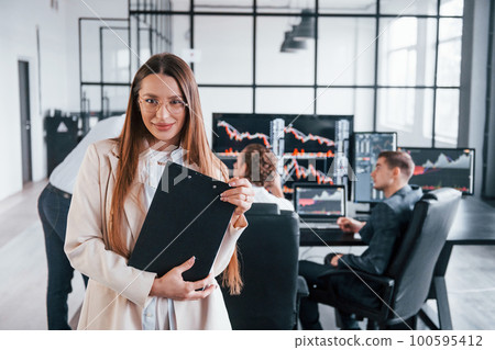 Female manager in front of colleguaes. Team of stockbrokers works in modern office with many display screens Female manager in front of colleguaes. Team of stockbrokers works in modern office with many display screens 100595412