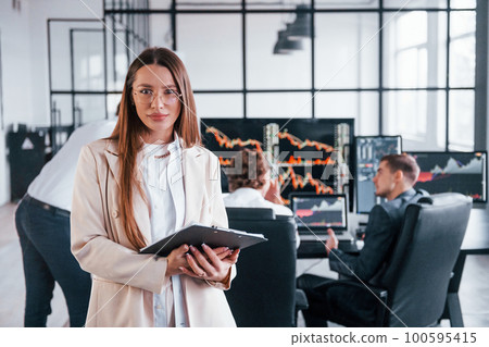 Female manager in front of colleguaes. Team of stockbrokers works in modern office with many display screens Female manager in front of colleguaes. Team of stockbrokers works in modern office with many display screens 100595415