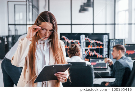Female manager in front of colleguaes. Team of stockbrokers works in modern office with many display screens Female manager in front of colleguaes. Team of stockbrokers works in modern office with many display screens 100595416