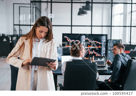 Female manager in front of colleguaes. Team of stockbrokers works in modern office with many display screens Female manager in front of colleguaes. Team of stockbrokers works in modern office with many display screens 100595417