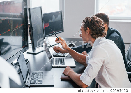 Attention to details. Team of stockbrokers works in modern office with many display screens 100595420