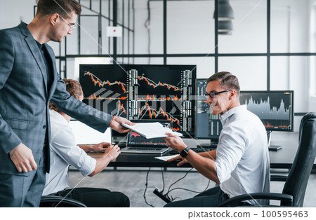With documents. Team of stockbrokers works in modern office with many display screens With documents. Team of stockbrokers works in modern office with many display screens 100595463