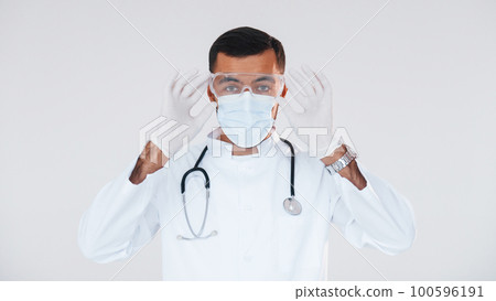 Medic in uniform. Young handsome man standing indoors against white background Medic in uniform. Young handsome man standing indoors against white background 100596191