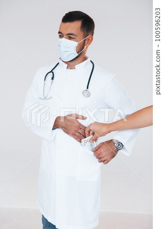 Medic holds money. Young handsome man standing indoors against white background 100596203