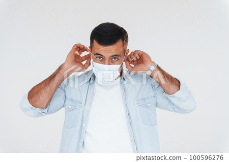 In protective mask. Young handsome man standing indoors against white background 100596276