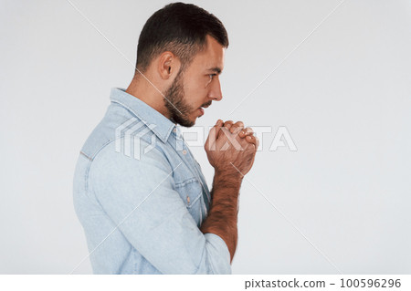 Guy is praying. Young handsome man standing indoors against white background 100596296