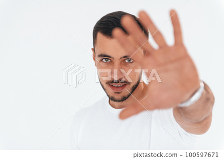Stop gesture. Young handsome man standing indoors against white background 100597671