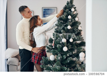 Standing near fir. Young romantic couple celebrates New year together indoors Standing near fir. Young romantic couple celebrates New year together indoors 100598704