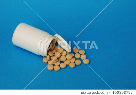Brown pills and a white jar on a blue background. 100598792