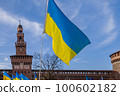 Flag with yellow and blue striped colors of Ukraine waving in the wind with a blue sky and sun. In the background the Castello Sforzesco in Milan. 100602182