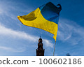 Flag with yellow and blue striped colors of Ukraine waving in the wind with a blue sky and sun. In the background the Castello Sforzesco in Milan. 100602186