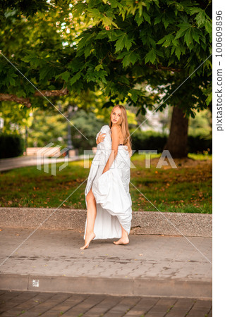Woman city blanket. Morning in the big city. A blonde woman in a white blanket is enjoying in the city center. Photographed for social media 100609896