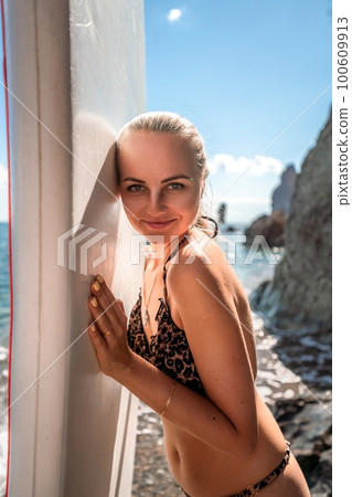 Woman in black bikini sap sea. Portrait of a happy girl on the background of a surfboard in the sea on a sunny summer day 100609913