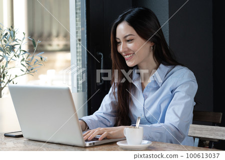 Young asian woman look at her laptop smiling near the window with coffee 100613037