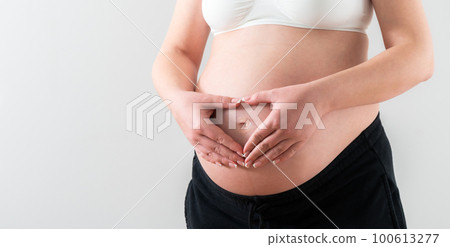 Hands folded in the shape of a heart on the middle of the belly of a pregnant girl 100613277