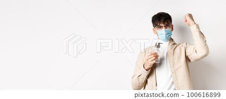 Health, covid and quarantine concept. Happy young man motivated to fight coronavirus, showing hand sanitizer and raising hand up in triumph, standing on white background Health, covid and quarantine concept. Happy young man motivated to fight coronavirus, showing hand sanitizer and raising hand up in triumph, standing on white background 100616899