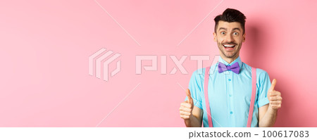 Excited caucasian guy showing thumbs up and praising great work, well done gesture, standing in suspenders and bow-tie on pink background 100617083