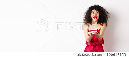 Holidays and celebration concept. Smiling woman in red dress giving you birthday cake with candle, standing over white background Holidays and celebration concept. Smiling woman in red dress giving you birthday cake with candle, standing over white background 100617153