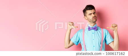 Serious and funny young man trying look cool, pointing at himself to self-promote, being a professional, standing over pink background Serious and funny young man trying look cool, pointing at himself to self-promote, being a professional, standing over pink background 100617162
