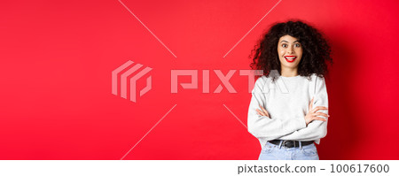 Cheerful young woman with curly hairstyle, raising eyebrows and looking surprised, hear interesting news, red background 100617600