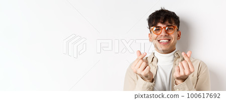 Cute young guy in glasses smiling and showing finger hearts, standing on white background Cute young guy in glasses smiling and showing finger hearts, standing on white background 100617692